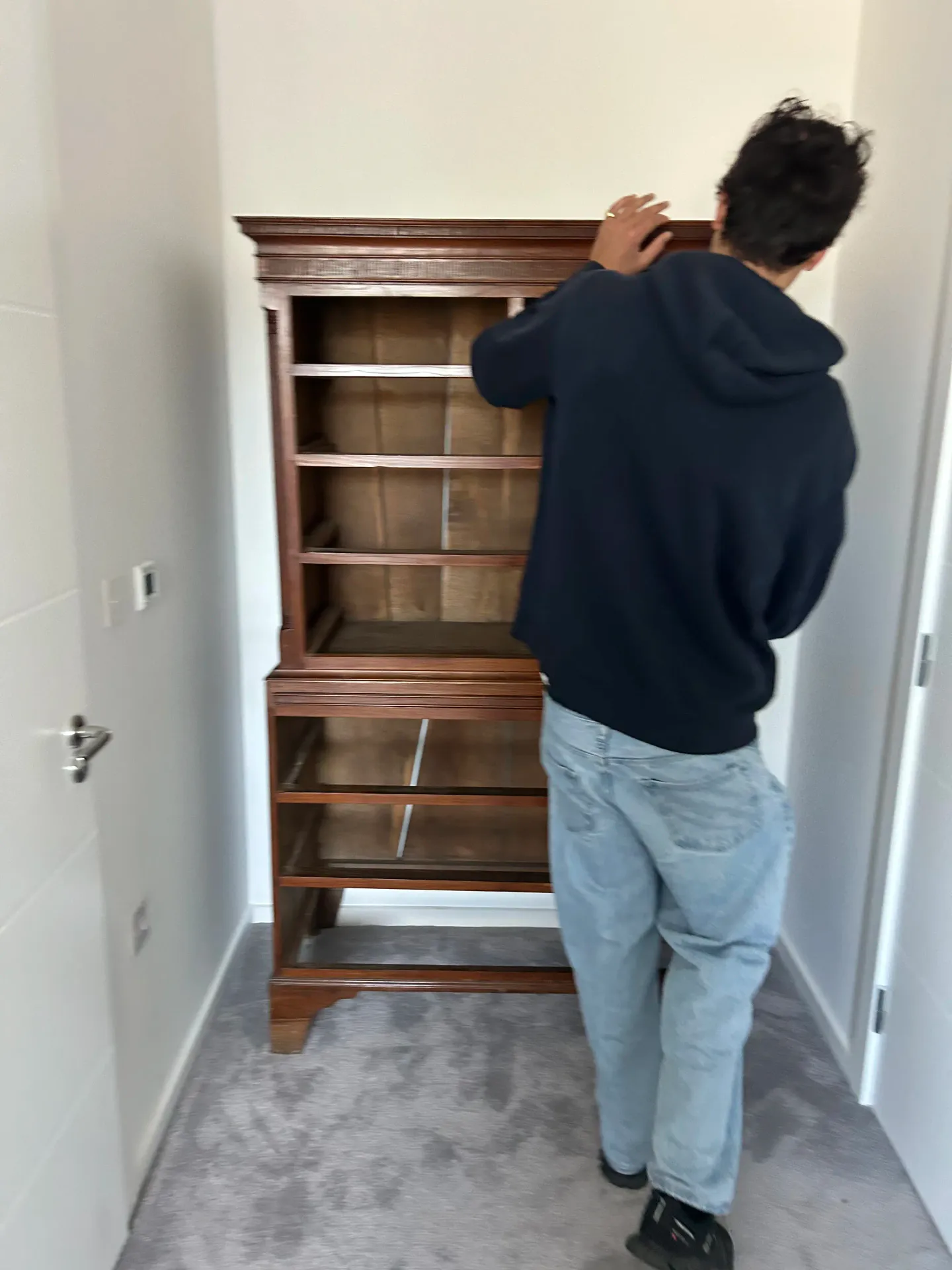 Next Removals team member setting a tall wooden cabinet in place in a customer's hallway