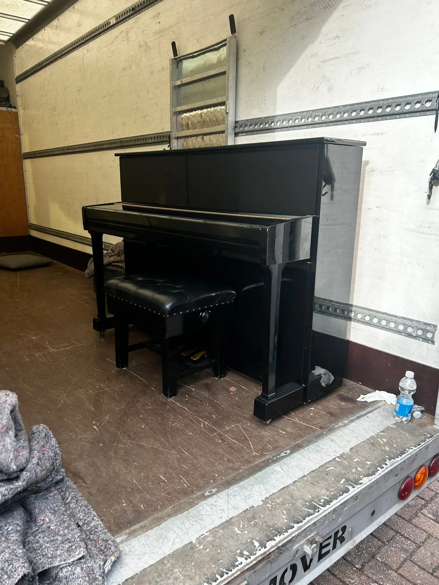 Black upright piano and its stool loaded in the back of the removals van