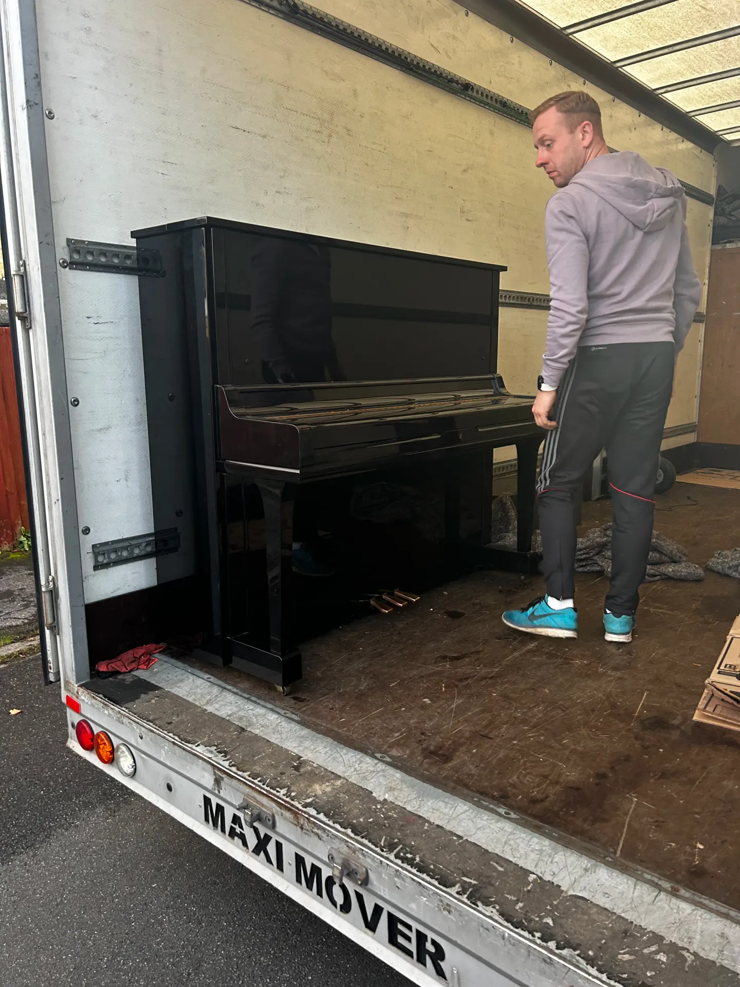 Next Removals team member loading a black upright piano into the van