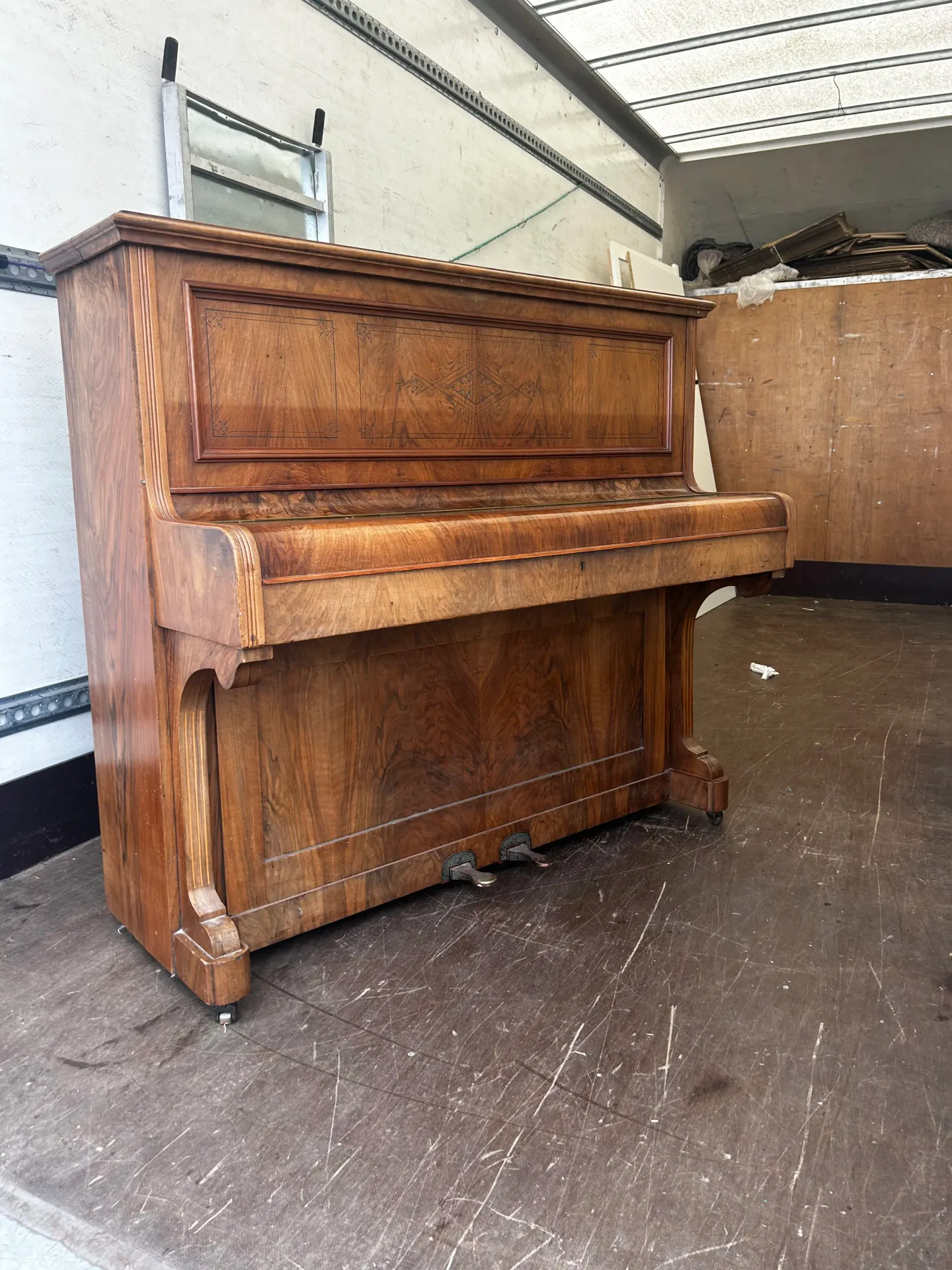 Walnut upright piano standing in the back of the removals van