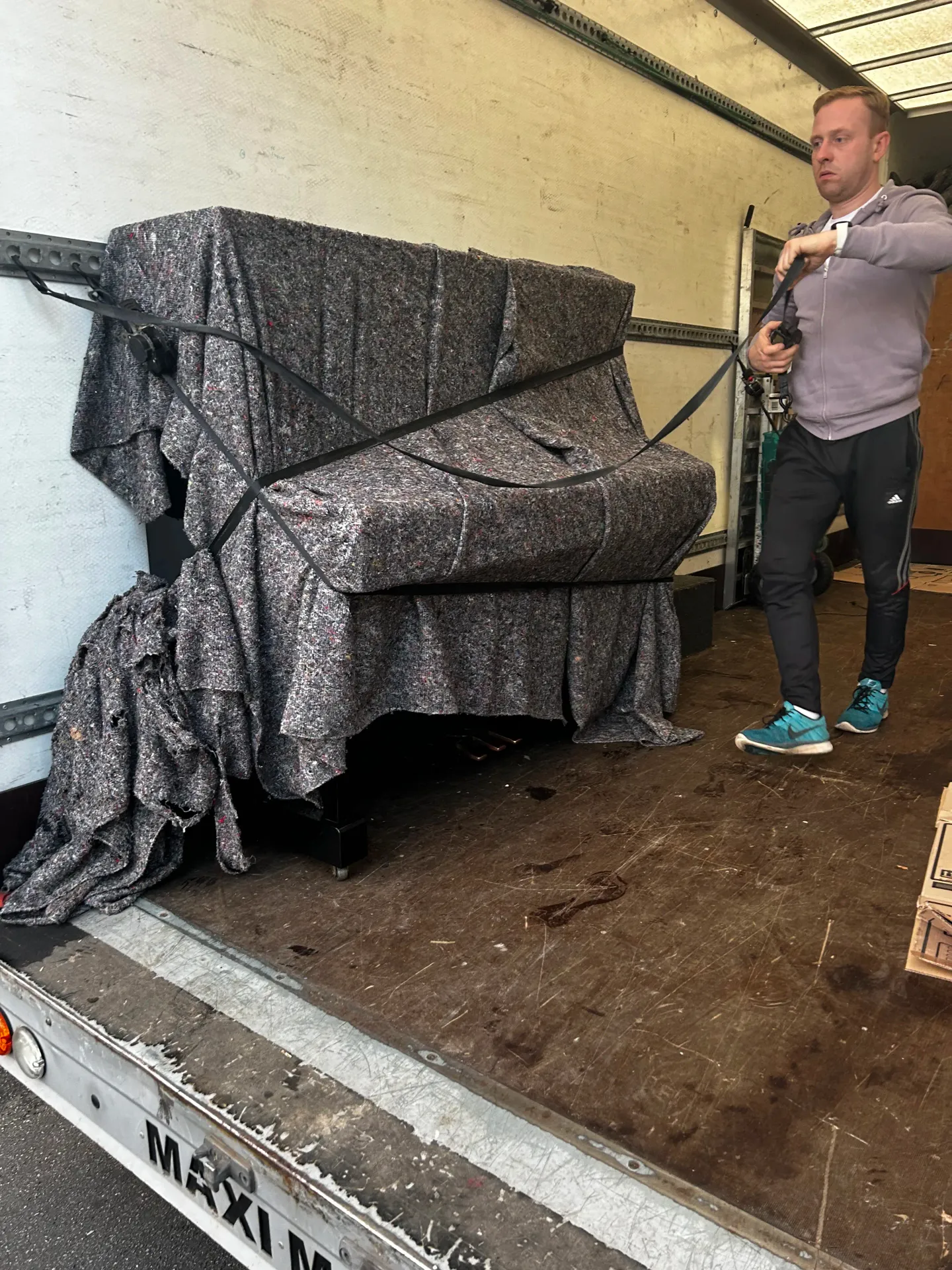 Next Removals team member strapping a blanket-wrapped piano to the side of the van