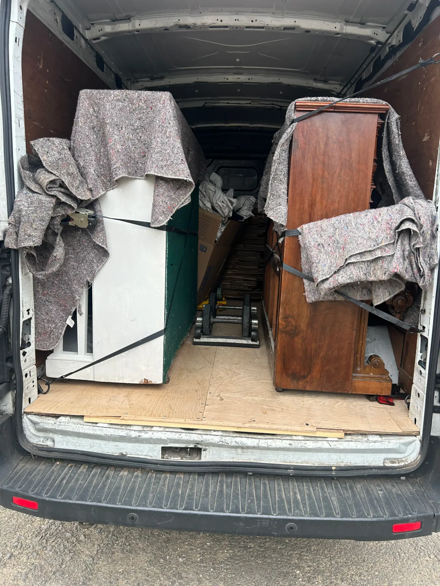 Two upright pianos wrapped in protective blankets and strapped in place inside a van